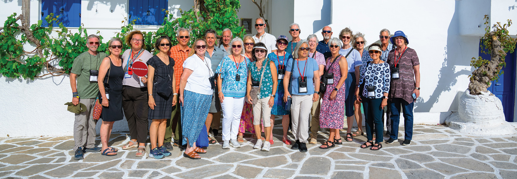 A group of Road Scholar participants smiles for a photo on a stone patio in front of a white building in Greece.