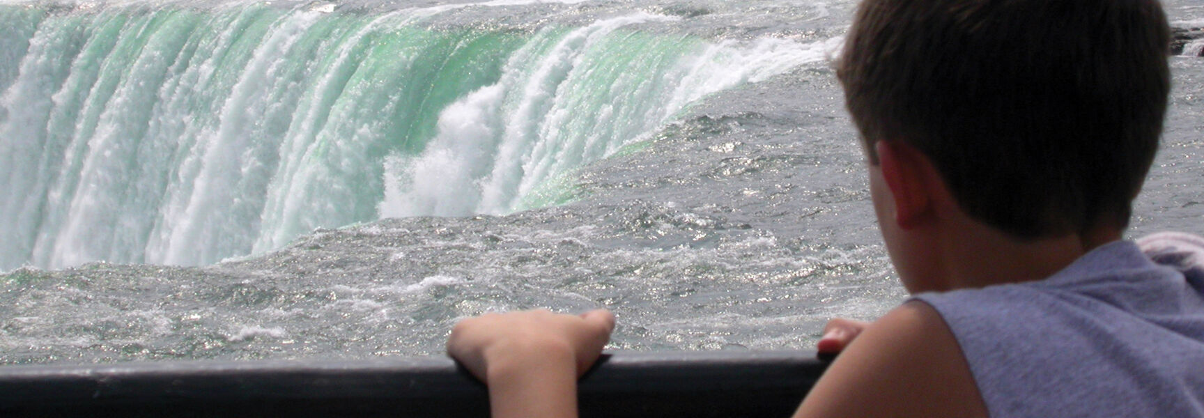 A young boy looks out over the rushing turquoise water of Niagara Falls in Ontario.