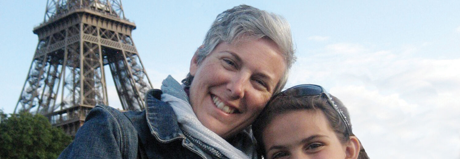 A woman and her grandchild smile together in front of the Eiffel Tower in Paris, France.