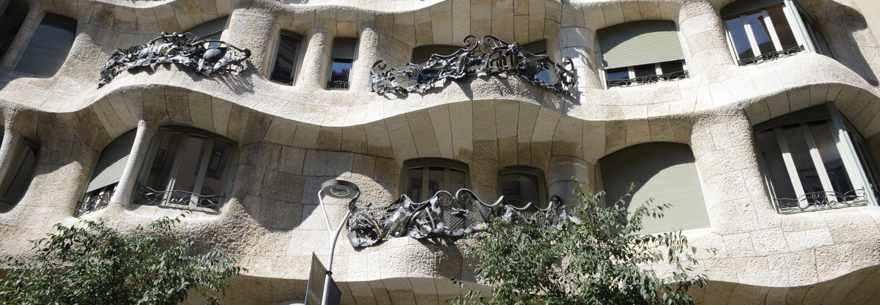 The sun shines on the undulating stone facade and ornate wrought-iron balconies of the Casa Milà building in Spain.