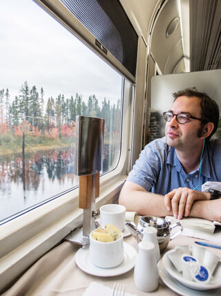 A traveler looks out a train window at colorful autumn foliage while journeying from Québec City toward the Canadian Maritimes.