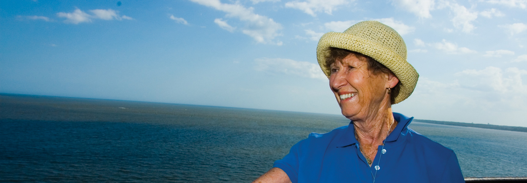 A woman in a straw hat smiles while looking out at the ocean off the coast of Georgia.