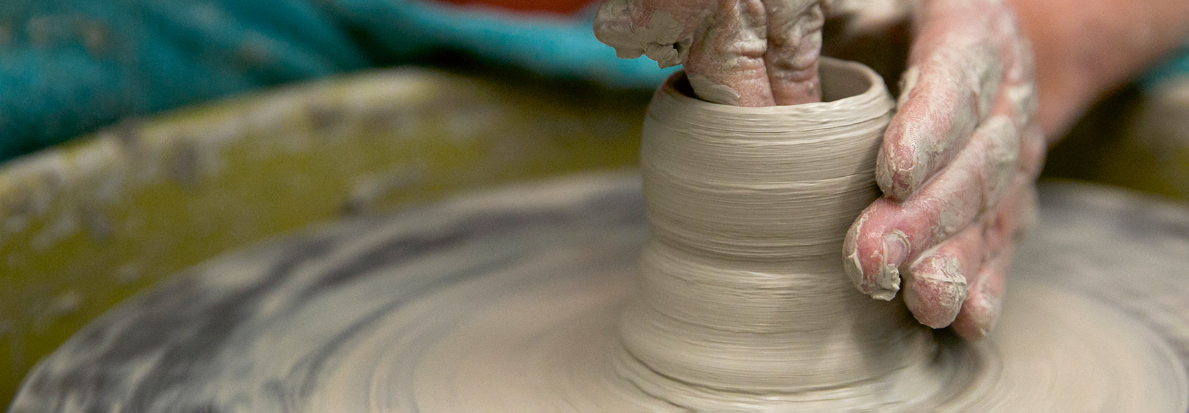 A person's hands covered in clay shape a pot on a spinning potter's wheel during a class in North Carolina.