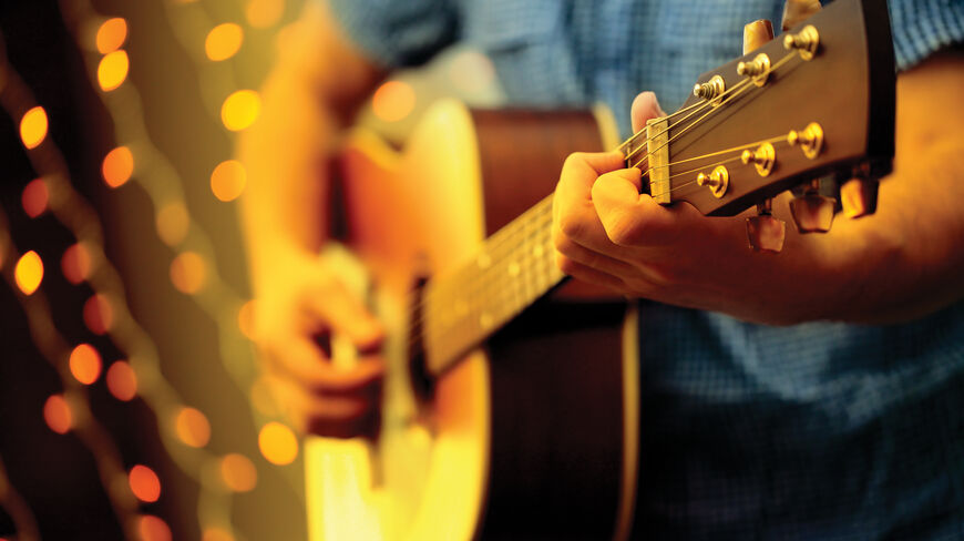 Close-up of a musician playing an acoustic guitar with glowing bokeh lights, representing the vibrant music scenes of Nashville, Memphis, and New Orleans.