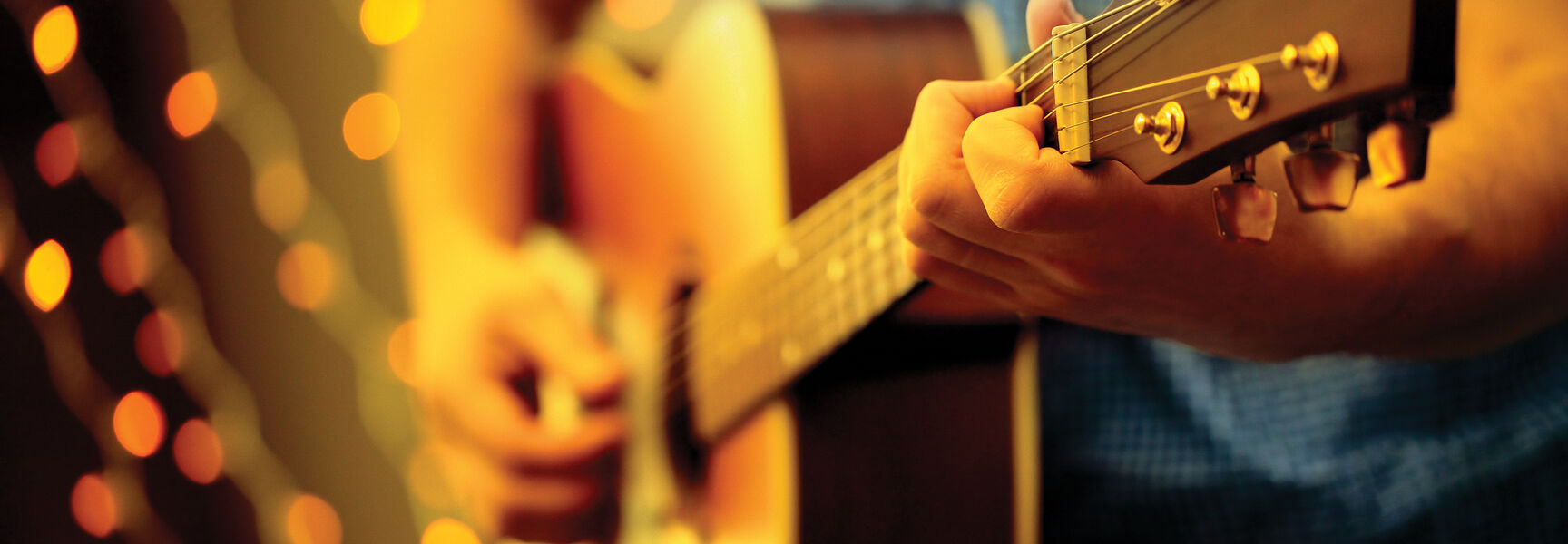 Close-up of a musician playing an acoustic guitar with glowing bokeh lights, representing the vibrant music scenes of Nashville, Memphis, and New Orleans.