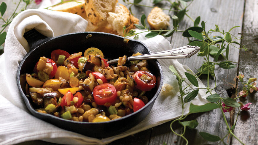A traditional Sicilian vegetable dish in a cast-iron skillet, served with crusty bread on a rustic wooden table during a cooking experience in Italy.