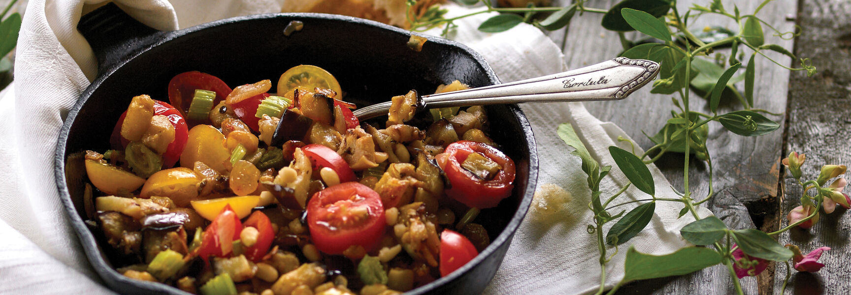 A traditional Sicilian vegetable dish in a cast-iron skillet, served with crusty bread on a rustic wooden table during a cooking experience in Italy.