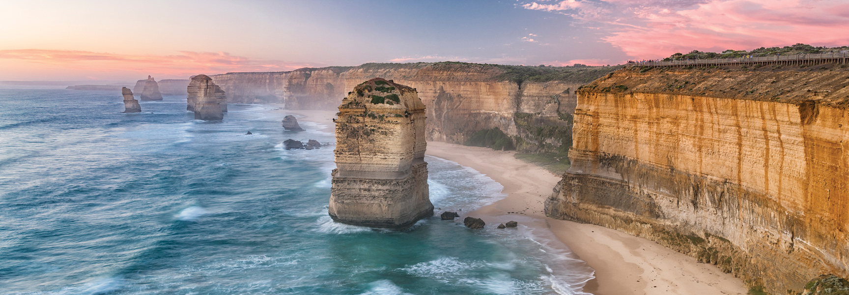 The Twelve Apostles sea stacks stand in the ocean off the coast of the Great Ocean Road in Australia at sunset.