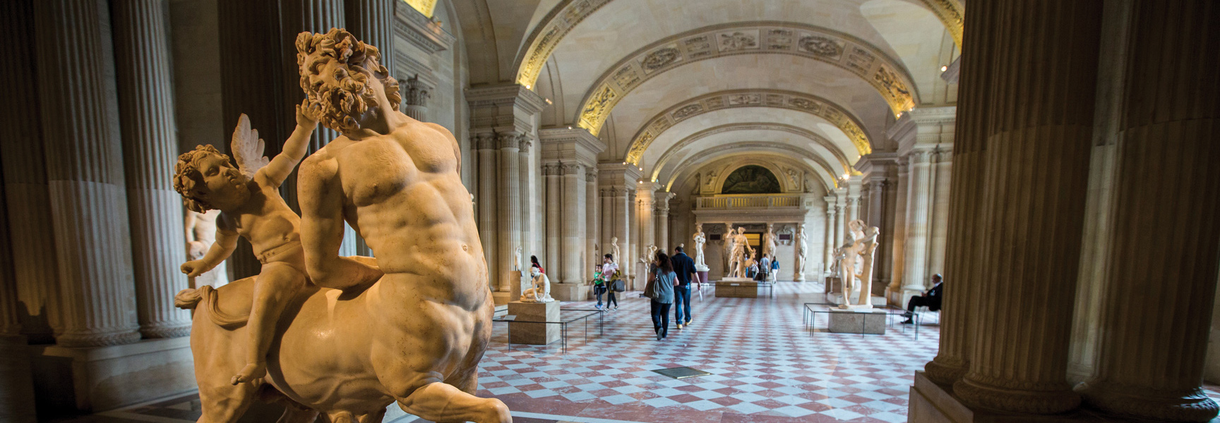 A marble statue of a centaur and cherub stands in a grand museum hall with high-arched ceilings and checkered floors in Paris, France.