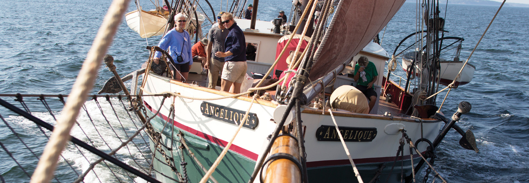 A group of people enjoy a sunny day on the deck of the large sailing vessel Angelique as it cruises off the coast of Maine.