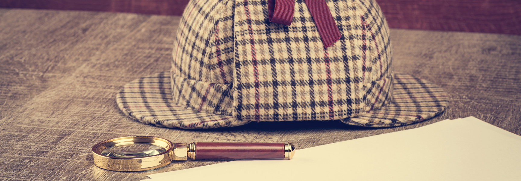 A Sherlock Holmes-style deerstalker hat and magnifying glass rest on a wooden desk.