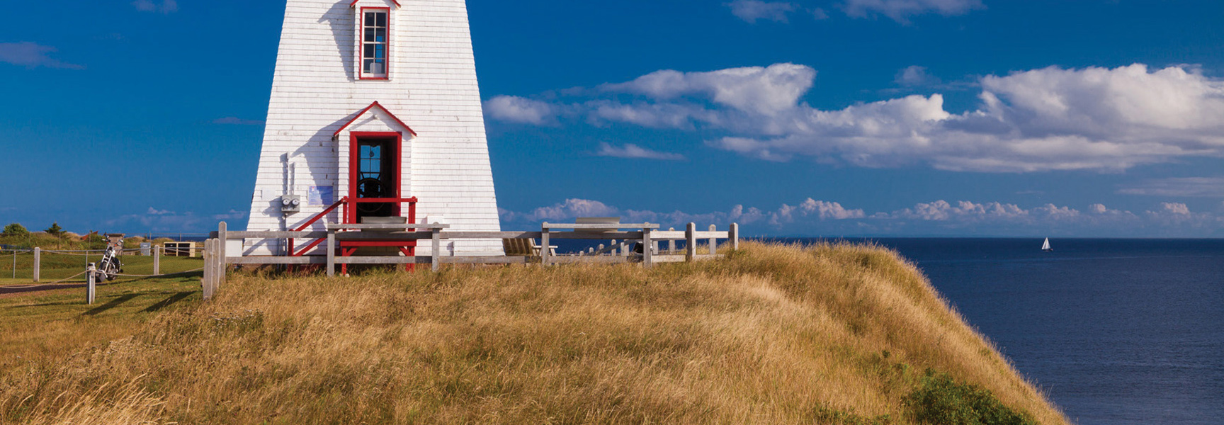 A white lighthouse with a red door sits on a grassy cliff overlooking the ocean on Prince Edward Island.
