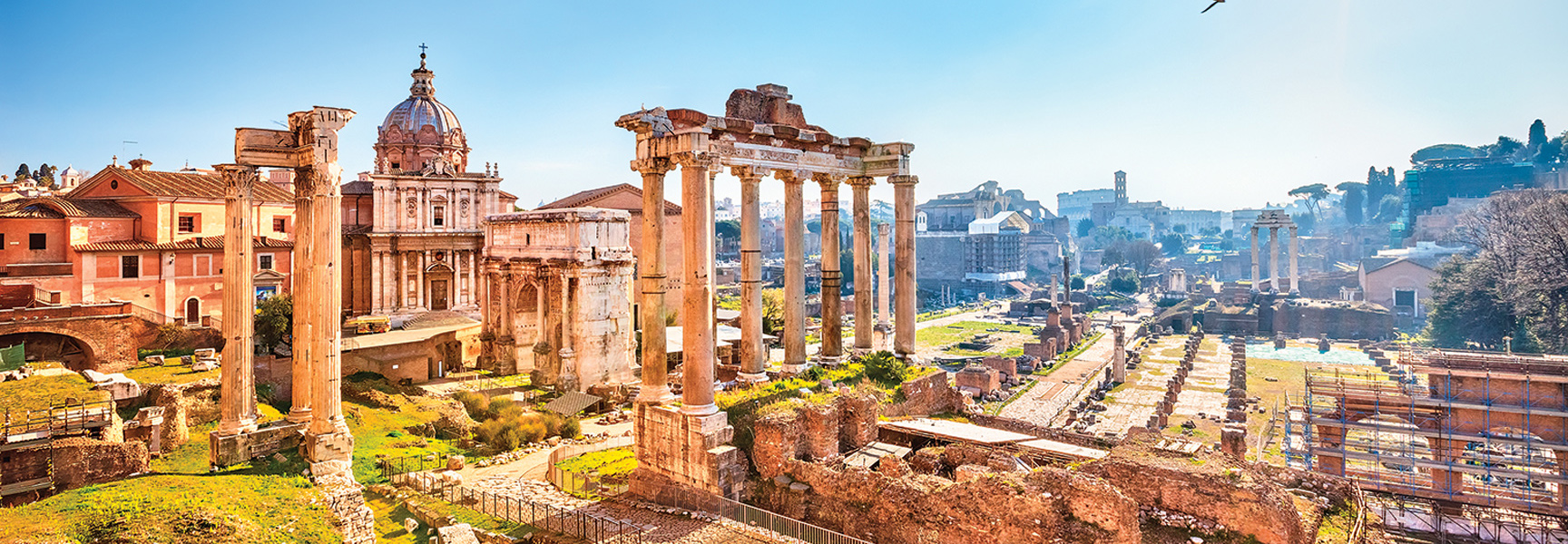 A sunny, panoramic view of the ancient Roman Forum ruins in Italy, featuring prominent columns and basilicas under a bright, clear sky.