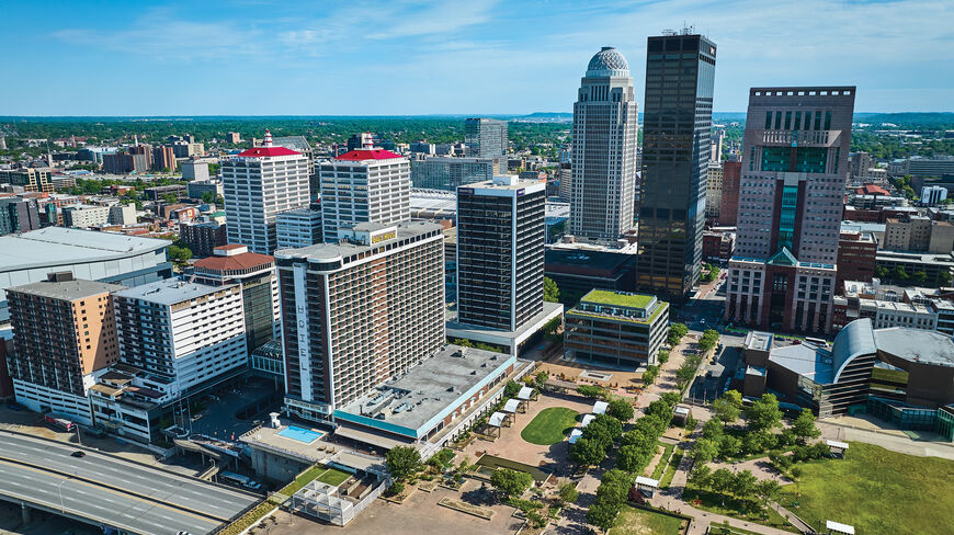 An aerial view of the downtown Louisville, Kentucky skyline featuring prominent skyscrapers and the Galt House Hotel under a clear blue sky.