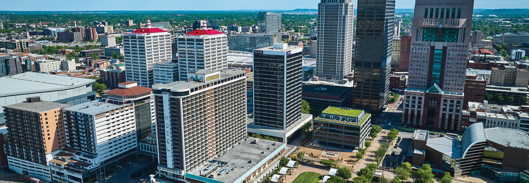 An aerial view of the downtown Louisville, Kentucky skyline featuring prominent skyscrapers and the Galt House Hotel under a clear blue sky.