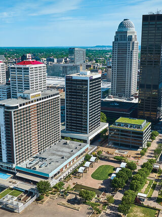 An aerial view of the downtown Louisville, Kentucky skyline featuring prominent skyscrapers and the Galt House Hotel under a clear blue sky.