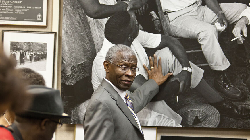 A guide in a suit gestures toward a large photograph of Martin Luther King Jr. during a Civil Rights Movement history tour in Georgia.