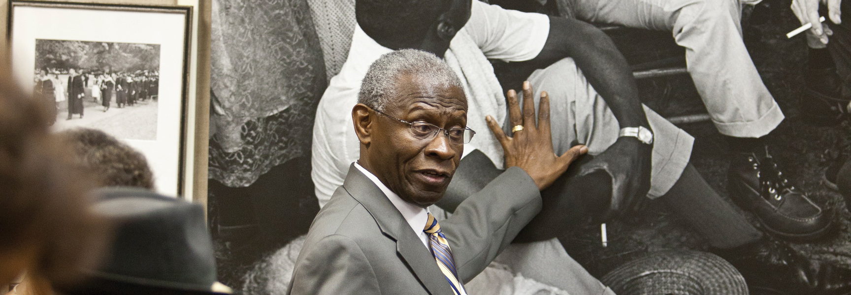 A man gestures to a large black-and-white photograph while speaking about the Civil Rights Movement in Georgia or Alabama.