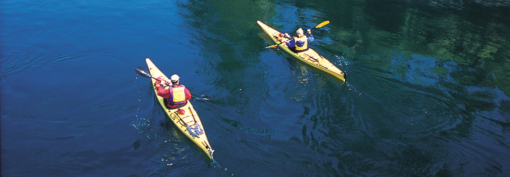 An aerial view of two people paddling yellow kayaks on the dark blue water of the Eastern Shore in Virginia.