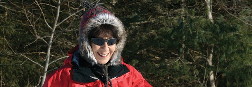 A woman in a red jacket cross-country skis through the snowy winter wonderland of the Adirondacks, New York.