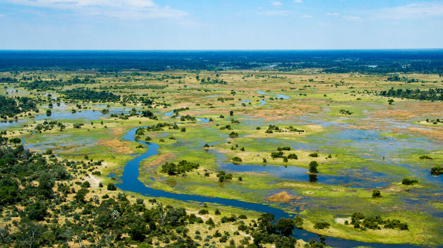 Aerial view of a winding blue river flowing through the lush green wetlands of the Okavanga Delta in Botswana.
