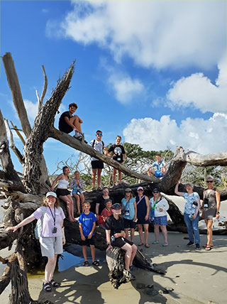 A group of adults and children pose for a photo on a large piece of driftwood on Driftwood Beach on Jekyll Island, Georgia.