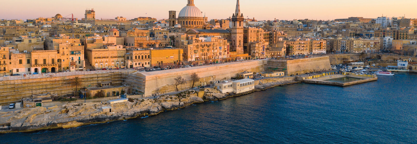 An aerial view of the historic skyline of Valletta, Malta, during winter, featuring the iconic dome and spire along the Mediterranean coastline.