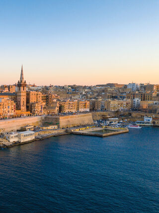 An aerial view of the historic skyline of Valletta, Malta, during winter, featuring the iconic dome and spire along the Mediterranean coastline.