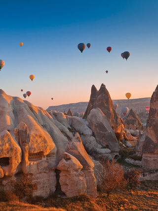 Hot air balloons float over the unique geological landscape and ancient cave dwellings of Cappadocia, Turkey, during a vibrant sunrise.