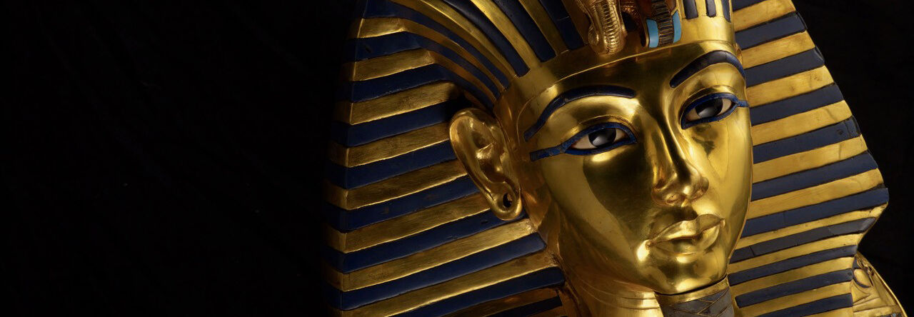 The ornate gold funerary mask of King Tutankhamun featuring blue lapis lazuli stripes and a false beard against a dark background.