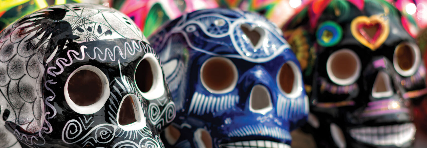 Ornately decorated ceramic skulls, symbols of the Day of the Dead tradition, are displayed in a row featuring vibrant patterns and intricate designs.