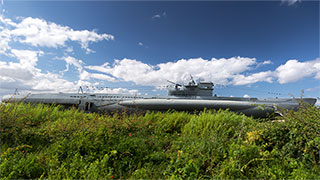 A German U-boat rests in a grassy field on a partly cloudy day, viewed from its port side.
