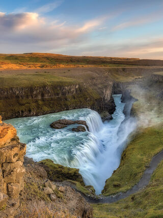 A massive waterfall cascades into a deep rocky canyon under a glowing sunset sky in the wilds of Iceland.