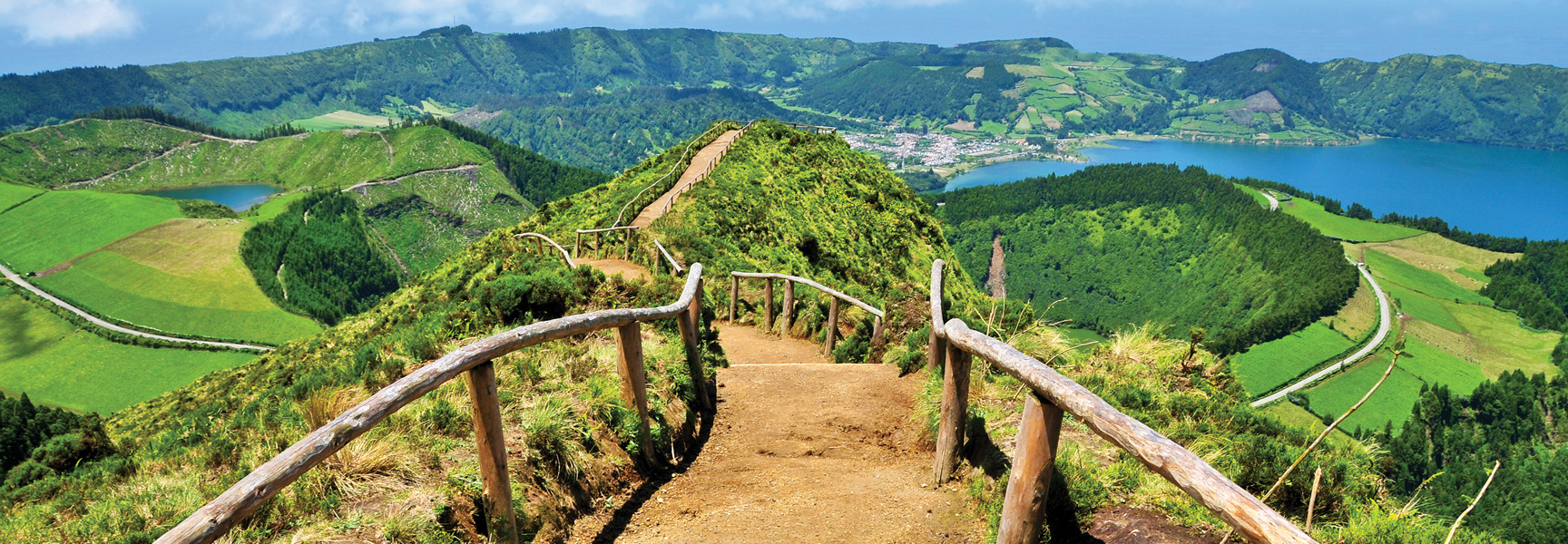 A scenic view from a hiking trail overlooking the lush green volcanic landscape and blue lakes of the Azores.