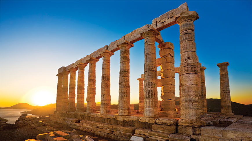 The ancient stone columns of the Temple of Poseidon at Cape Sounion, Greece, are lit by the setting sun overlooking the sea.