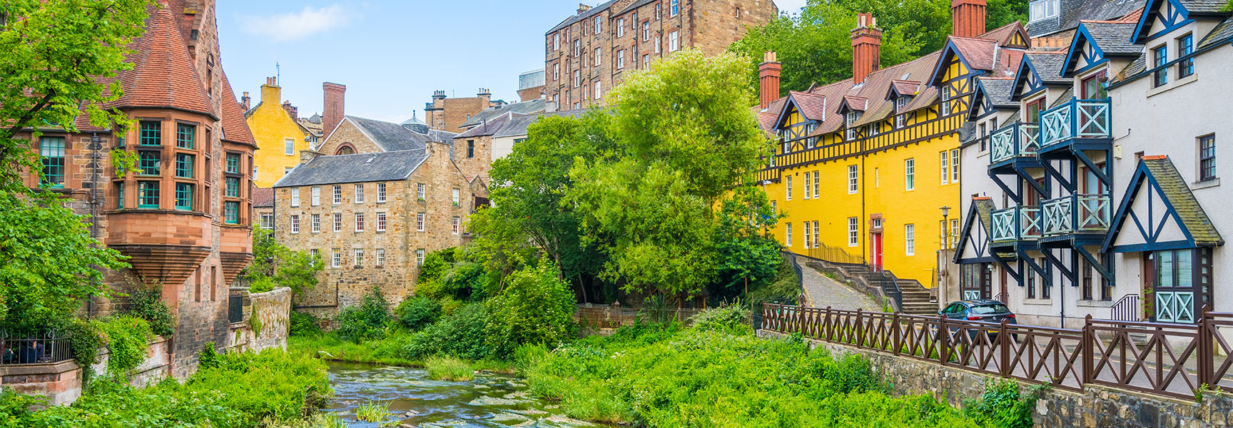 Scenic historic stone houses and lush green trees line the river in Edinburgh's picturesque Dean Village.