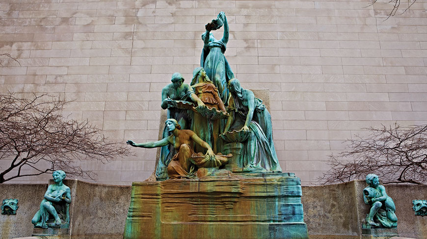 The Spirit of the Great Lakes Fountain, a multi-figured bronze sculpture, stands in front of a stone building in Chicago, Illinois.