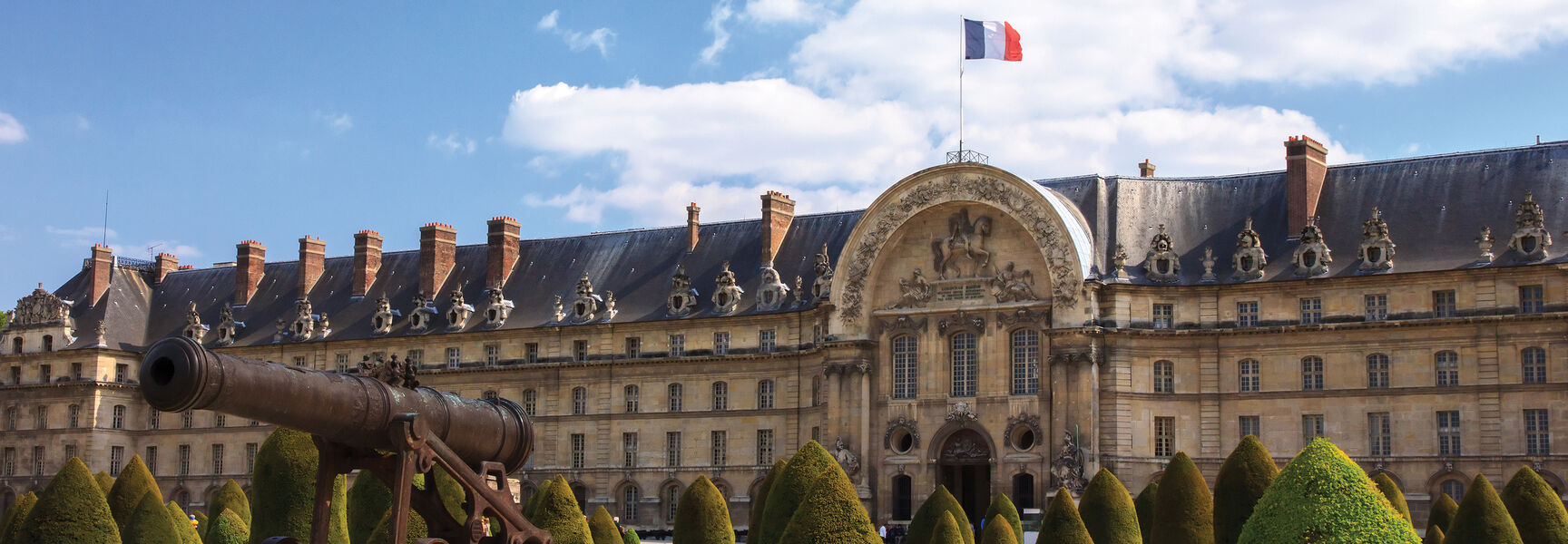 A historic French building with a cannon and the national flag, signifying locations associated with D-Day and the Allied Victory in France.