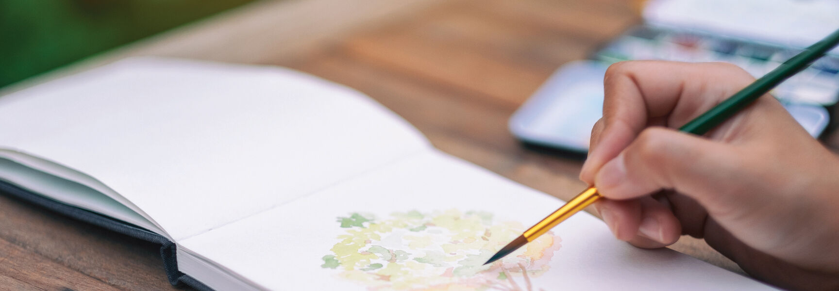A person paints a watercolor tree in a sketchbook during an intermediate watercolor workshop in the Laurel Highlands of Pennsylvania.