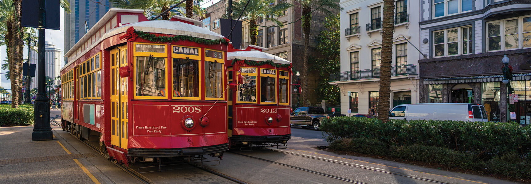 Two red and yellow streetcars travel along the tracks on a palm-lined street in downtown New Orleans, Louisiana.