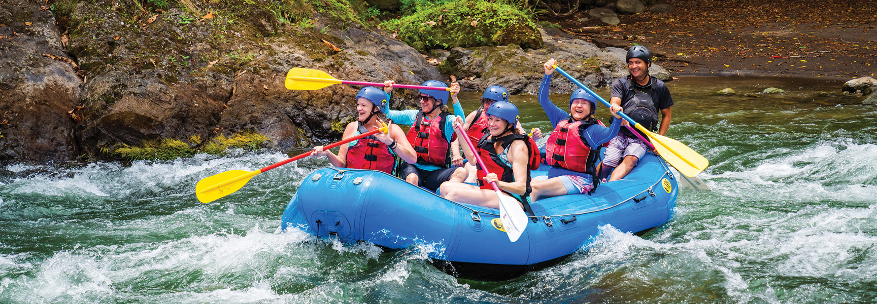 A group of women laugh as they paddle a raft down a river during a whitewater rafting trip in Costa Rica.