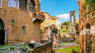 Ancient Roman ruins and historic brick buildings within the Rome Jewish Ghetto archaeological area under a sunny blue sky.