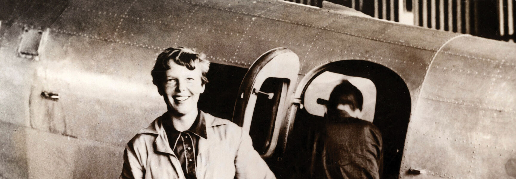 Amelia Earhart smiles while standing in front of her Lockheed Electra airplane during her 1937 attempt to fly around the world.