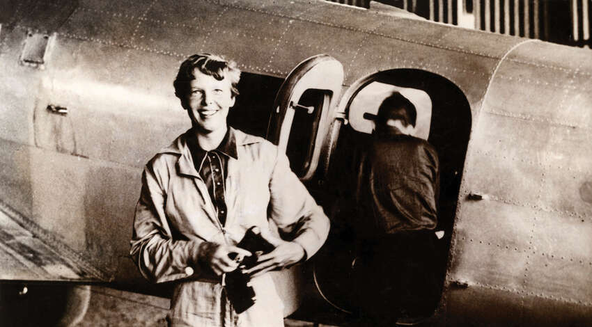 Amelia Earhart smiles while standing in front of her Lockheed Electra airplane during her 1937 attempt to fly around the world.
