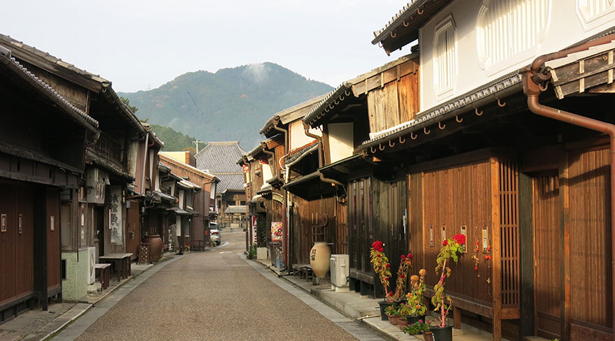 Traditional wooden buildings line the historic Tokaido Trail in Kameyama township, Japan, with a mountain peak rising in the background.