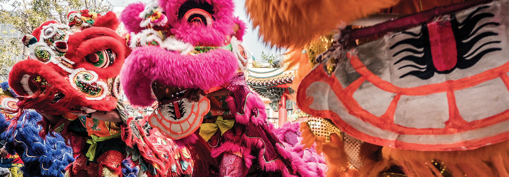 Vibrant, colorful lion dancers perform in front of a traditional Chinese building during a Chinese New Year celebration.