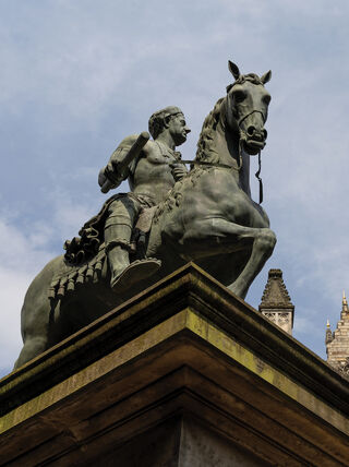 Bronze equestrian statue representing the Scottish monarchy stands against a blue sky before the gothic architecture of a cathedral, reflecting rich Scottish history.