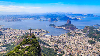 An aerial view of Rio de Janeiro, Brazil, showing the Christ the Redeemer statue overlooking the city, Sugarloaf Mountain, and Guanabara Bay.