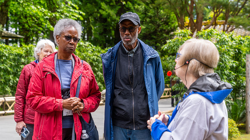 A group of people listen to a guide wearing a headset during a tour of the Portland Japanese Garden in Oregon.