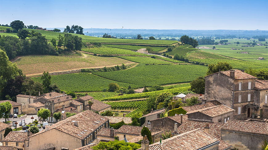 Rolling green Saint-Émilion vineyards overlooking a historic village with stone buildings and terracotta tile roofs in the French countryside.